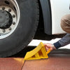 A hand places a yellow heavy duty car wheel chock anti-slip tire stop block under a car tire.