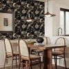 A dining room setting featuring a wooden table and chairs with a dark floral wallpaper backdrop.