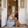A young girl sits on the floor with a golden retriever in a bright interior next to a white door frame.