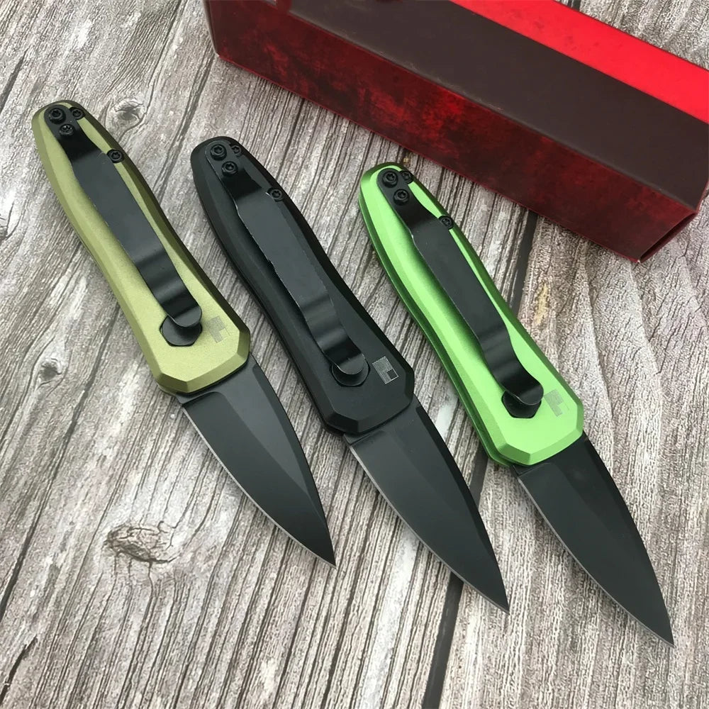 Une paire de couteaux de survie pliants compacts avec poignées noires et lames vertes posés sur une surface en bois à côté d'