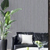 A potted plant stands next to a black leather sofa with white pillows against a gray vertical striped wall.
