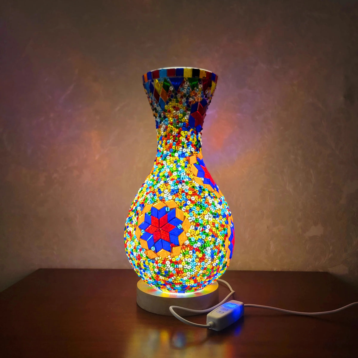 Una lámpara de mesa de vidrio multicolor y entrelazado con mosaico vibrante sobre una superficie de madera.