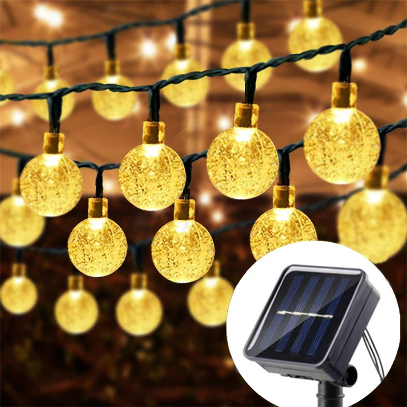 String lights with yellow glowing orbs hanging against a dark background, next to a solar panel.