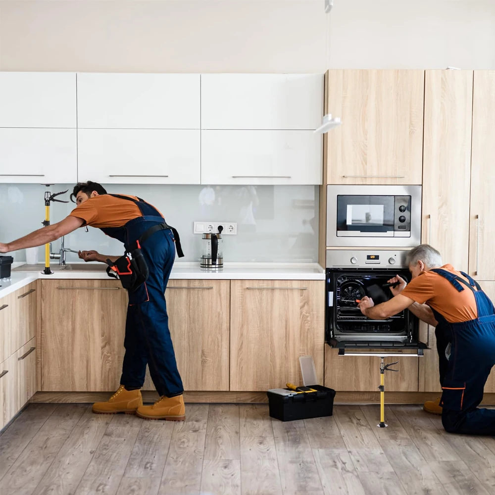 A man in an orange shirt is adjusting adjustable telescopic support rods on kitchen cabinets and appliances.