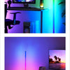 An RGB corner floor lamp illuminates a room, casting vibrant light onto a desk setup and a television screen.