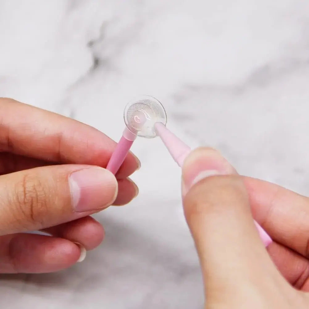 A hand holds a pink contact lens tool kit with multiple tips against a white marble background.