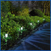 A row of solar powered outdoor garden lanterns lining a dark pathway through lush green foliage at night.