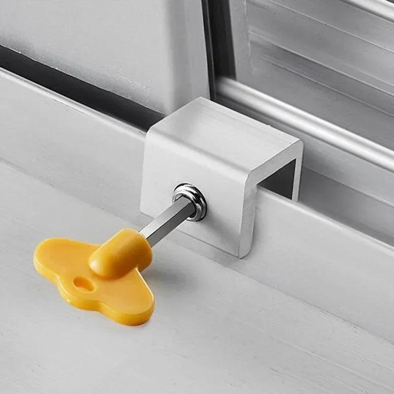 A yellow sliding window sash lock stopper is installed in a white window frame.