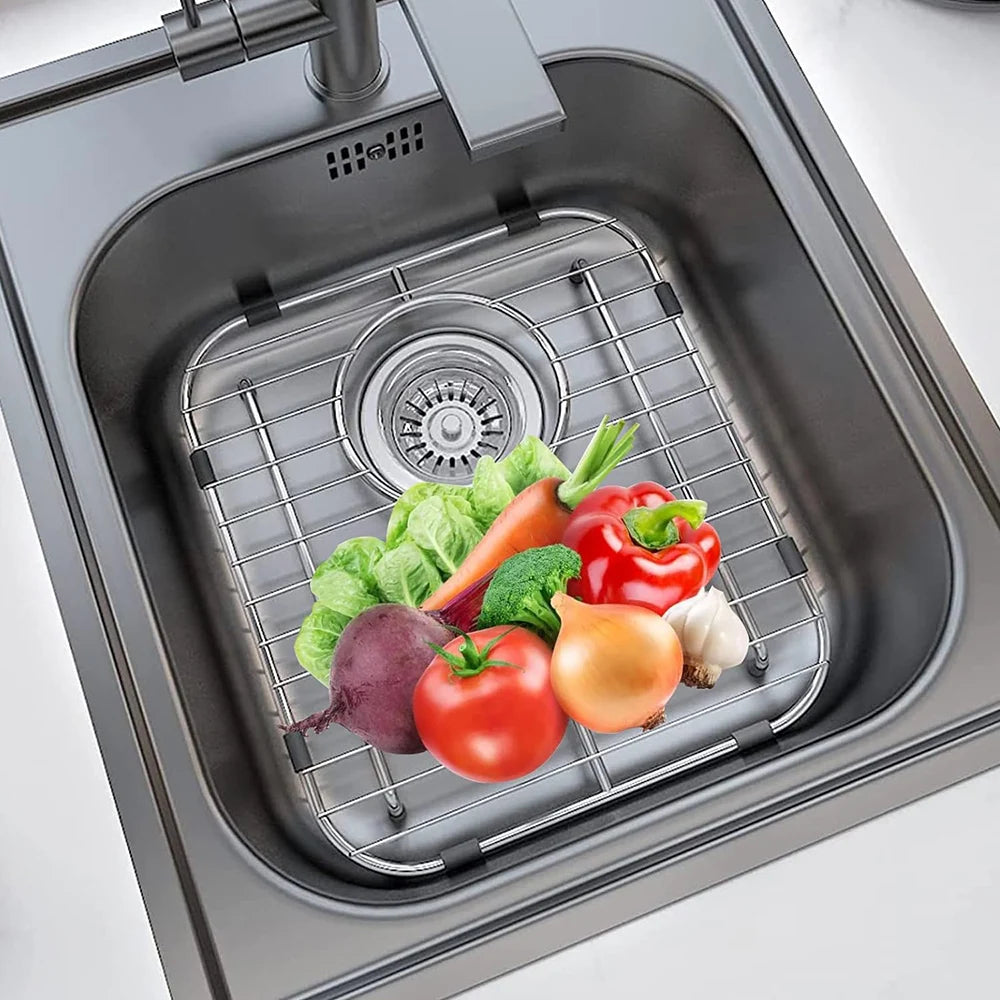 A stainless steel grid inside a sink protector is holding various fresh vegetables like tomatoes, peppers, and carrots.