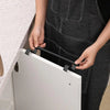 A person is installing a black stainless steel over cabinet towel rack onto a white cabinet door.