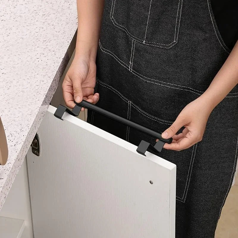 A person is installing a black stainless steel over cabinet towel rack onto a white cabinet door.