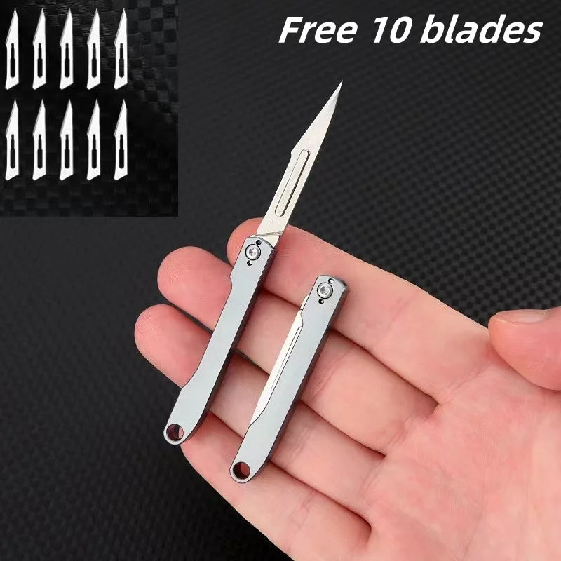 A hand holds a silver mini folding art knife with ten spare blades visible in the background.