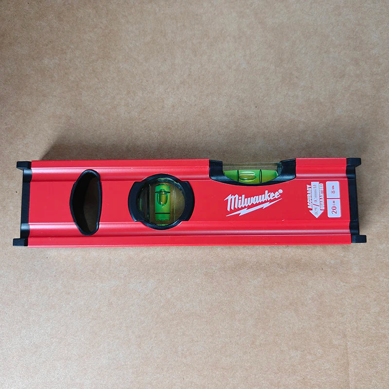 A red Milwaukee torpedo level set with a green liquid and a black viewing window on a brown background.
