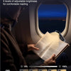 A person reads a book using a rechargeable light in an airplane window, demonstrating wider light coverage.