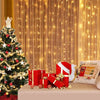 Festliche Weihnachts-Szene mit geschmücktem Weihnachtsbaum, Lichtern und Geschenken vor einem warmen Vorhanghintergrund.