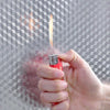 Une main tient un objet rouge avec une flamme, montrant des autocollants muraux en aluminium adhésifs.