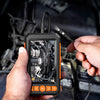 A hand holds an industrial waterproof borescope inspection camera displaying an internal view of an engine or appliance.