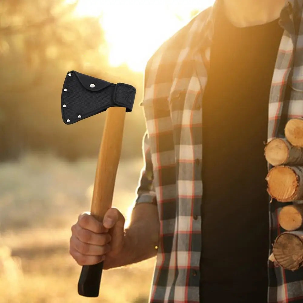 A hand holds a wooden handle with a black nylon axe blade cover in warm outdoor light.