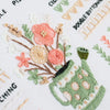 A close-up of a beginner embroidery kit featuring floral designs in pink, orange, and green thread on white fabric.