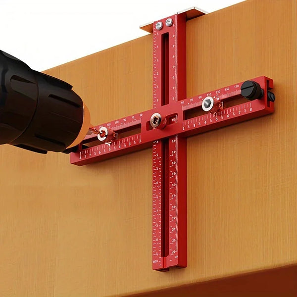 A red adjustable cabinet handle punch locator guide is mounted on a wooden surface, showing measurement markings.