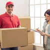 A man in a red shirt holds a cardboard box while a woman measures jewelry with a precision plastic ring sizer.