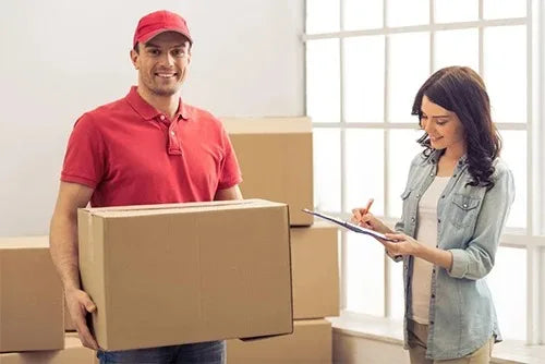A man in a red shirt holds a cardboard box while a woman measures jewelry with a precision plastic ring sizer.