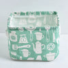A light green fabric storage basket with handles filled with various white kitchen utensils and tools.