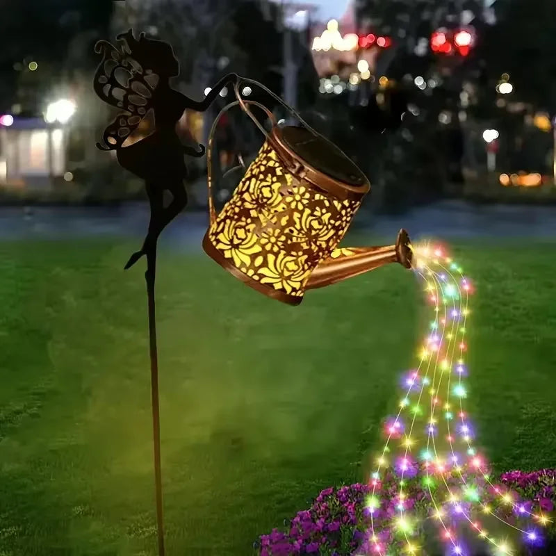 A silhouette of a fairy holding a glowing watering can light that shoots sparkling lights across the grass.