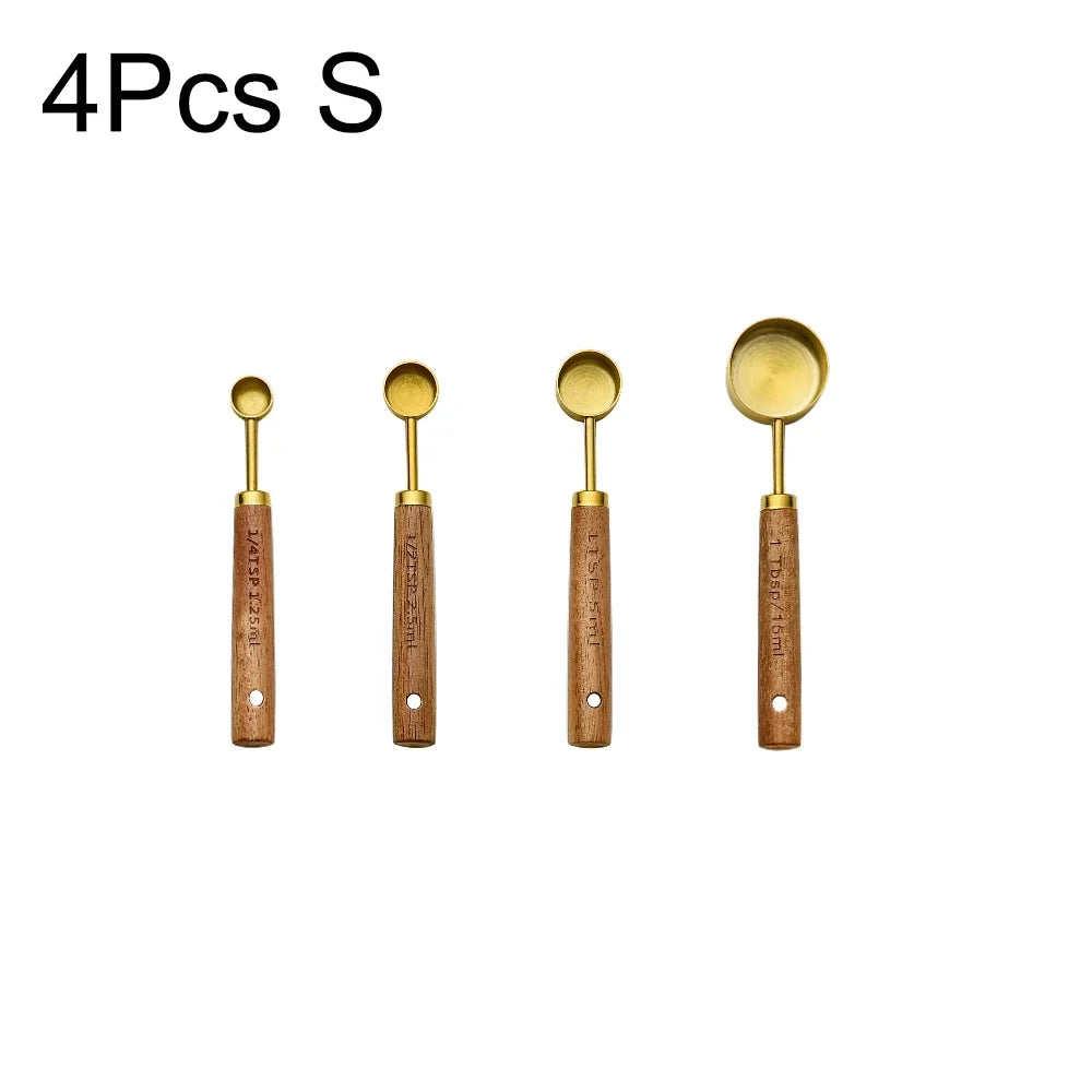 A set of four stainless steel and wooden measuring spoons with gold-colored heads.