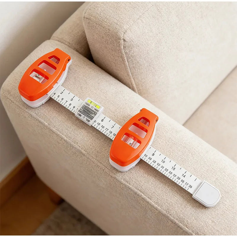 An orange precision picture hanging level and angle measuring tool is laid across a beige sofa cushion.