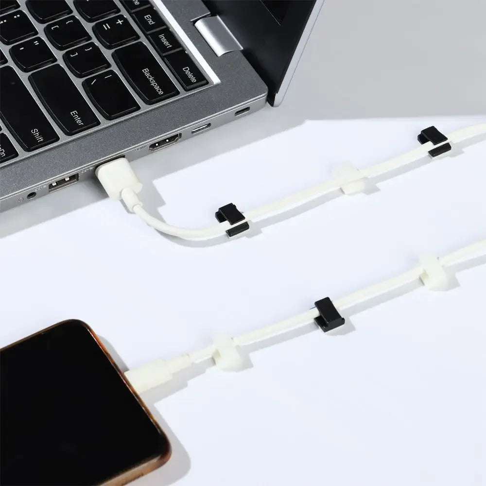 A close-up view of white self-adhesive cable clips used for cord organization near a laptop keyboard and smartphone.