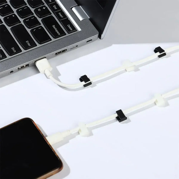 A close-up view of white self-adhesive cable clips used for cord organization near a laptop keyboard and smartphone.