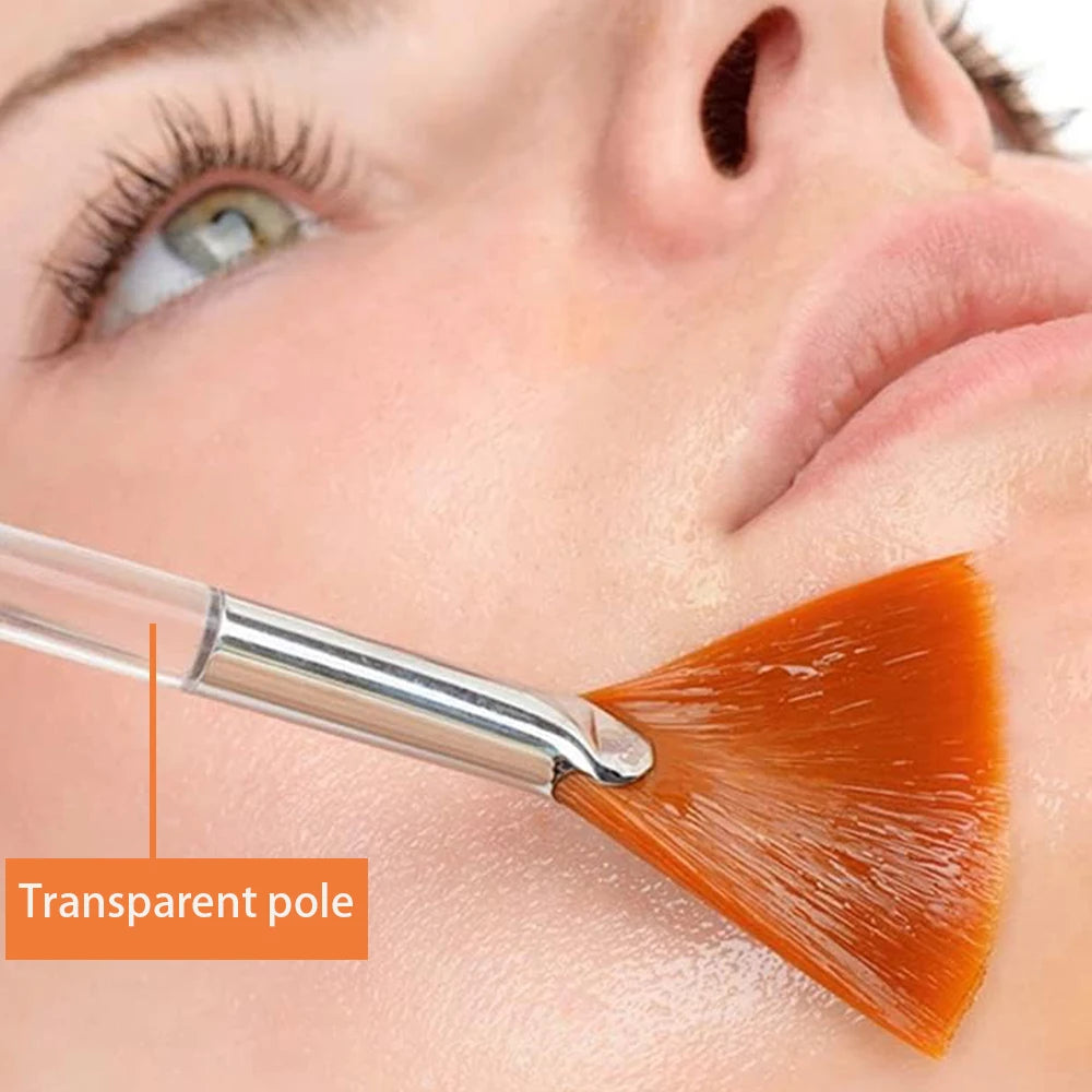 Brosse de masque facial en silicone avec tige transparente et poils orange appliquant le produit sur la peau.