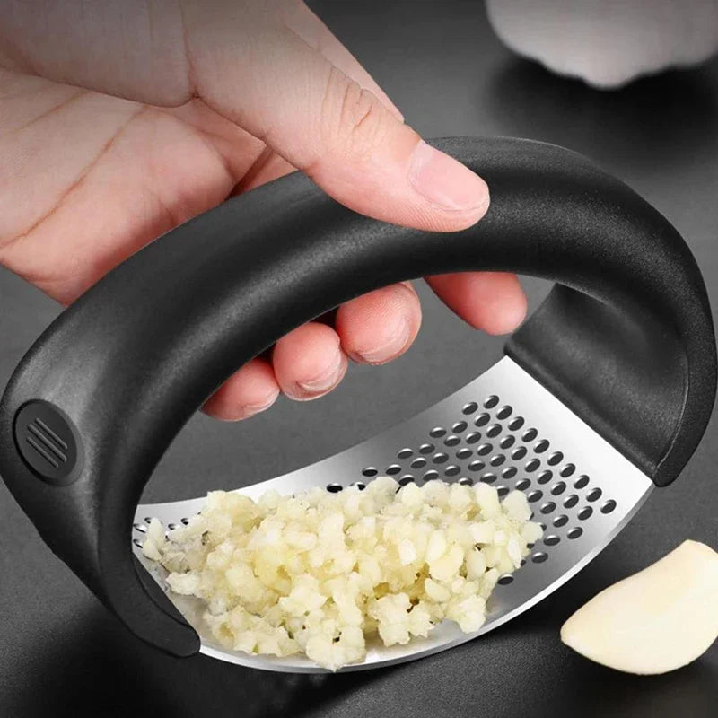 A hand is pressing minced garlic and ginger through a manual stainless steel press.