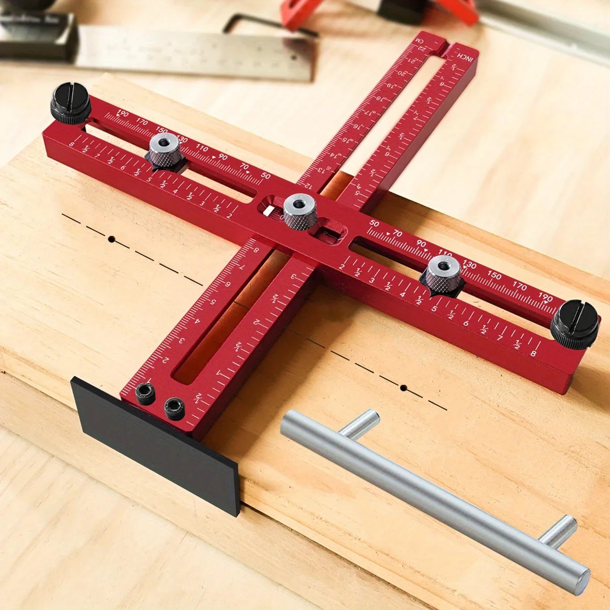 A red adjustable cabinet handle punch locator guide tool resting on a wooden surface with a metal rod.