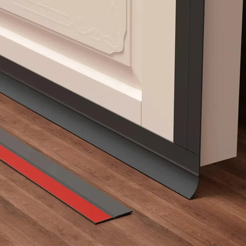 A close-up view of door draft stopper seal strips installed along the bottom edge of a door frame on a wooden floor.