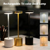 Three rechargeable tri-color desk lamps in silver, gold, and black sitting on a white surface.