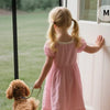 A young girl in a pink dress is interacting with a magnetic screen door on a white door frame.