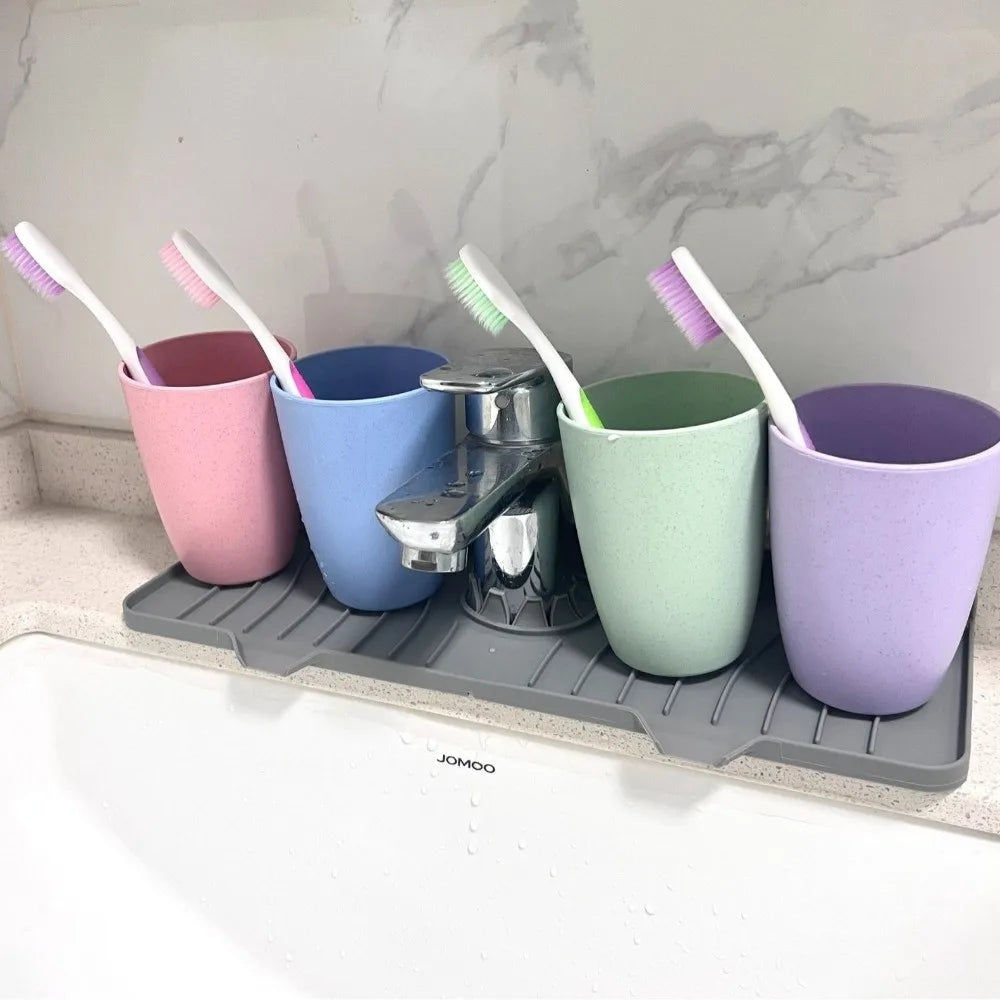 Une rangée de brosses en silicone colorées (rose, bleu, vert, violet) sont présentées dans des tasses en céramique gris