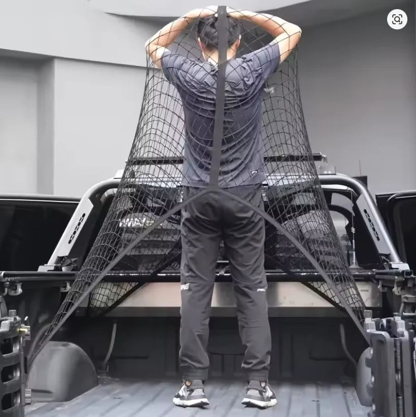 A person is standing inside a black cargo net organizer, looking down at their hands.