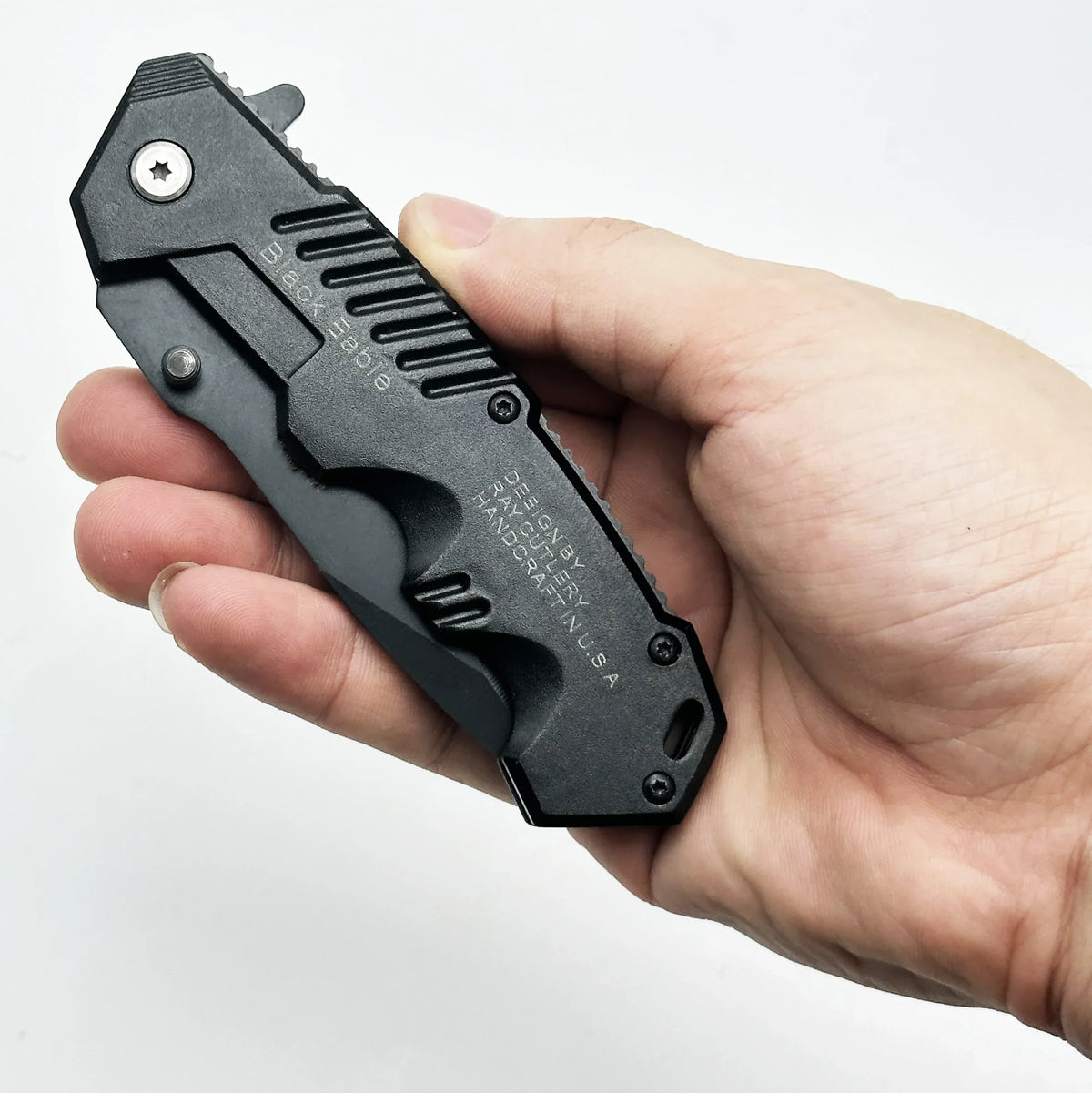 A hand holds a black folding survival knife with a textured handle and a silver star detail.
