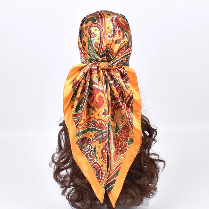 Foulard hijab en soie satinée carrée, motif paisley orange et or, attaché autour d'une perruque brun foncé.