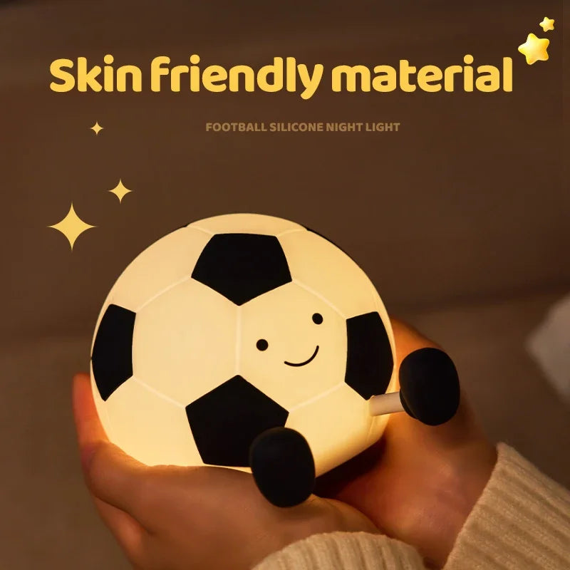 A glowing soccer ball silicone night light is held in a person's hand against a dark background.