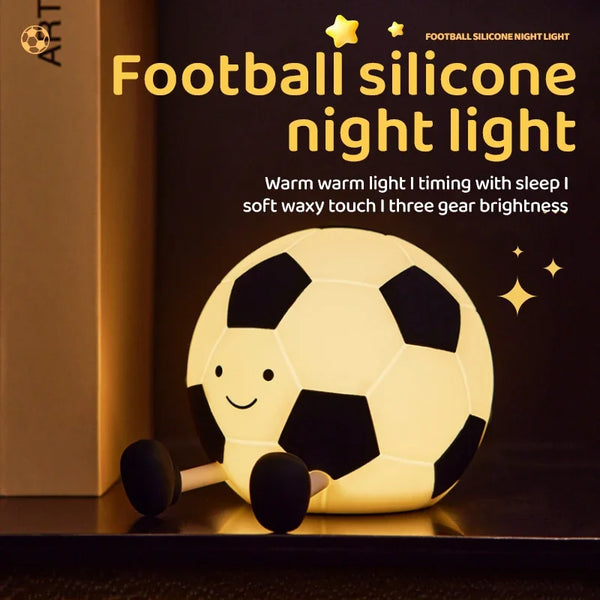 A yellow silicone football night light illuminating a soccer ball shape on a dark surface.