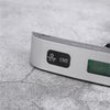 A silver portable digital weighing scale with a power button and display screen resting on a gray surface.