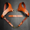 A pair of brown leather double shoulder suspenders laid out on a dark background.