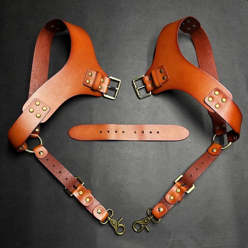 A pair of brown leather double shoulder suspenders laid out on a dark background.