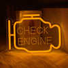 An oil change neon sign shaped like an engine, glowing orange, resting on a textured surface.