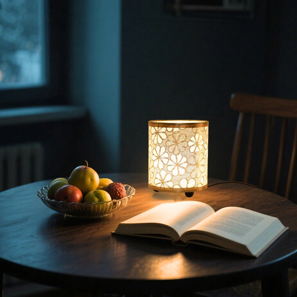 A minimalist desk lamp with a printed fabric shade illuminates an open book on a dark wooden table.