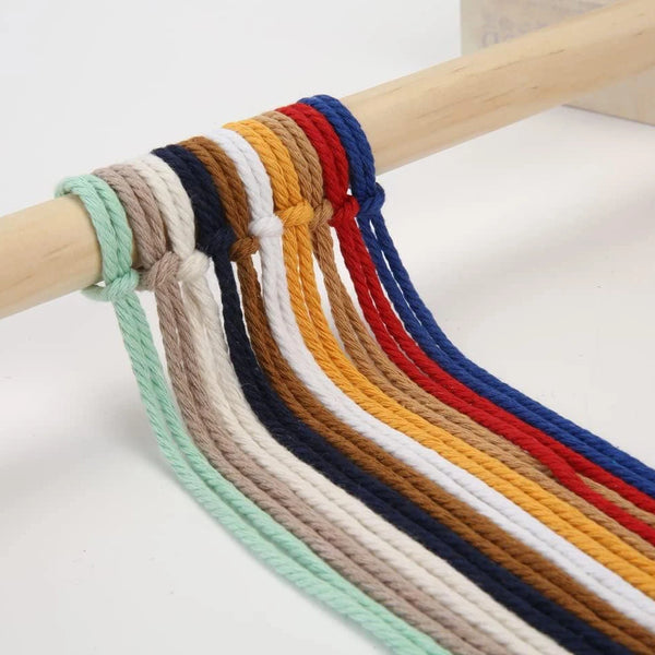 A close-up of a 100m natural cotton macrame cord with multiple colored strands hanging from a wooden dowel.
